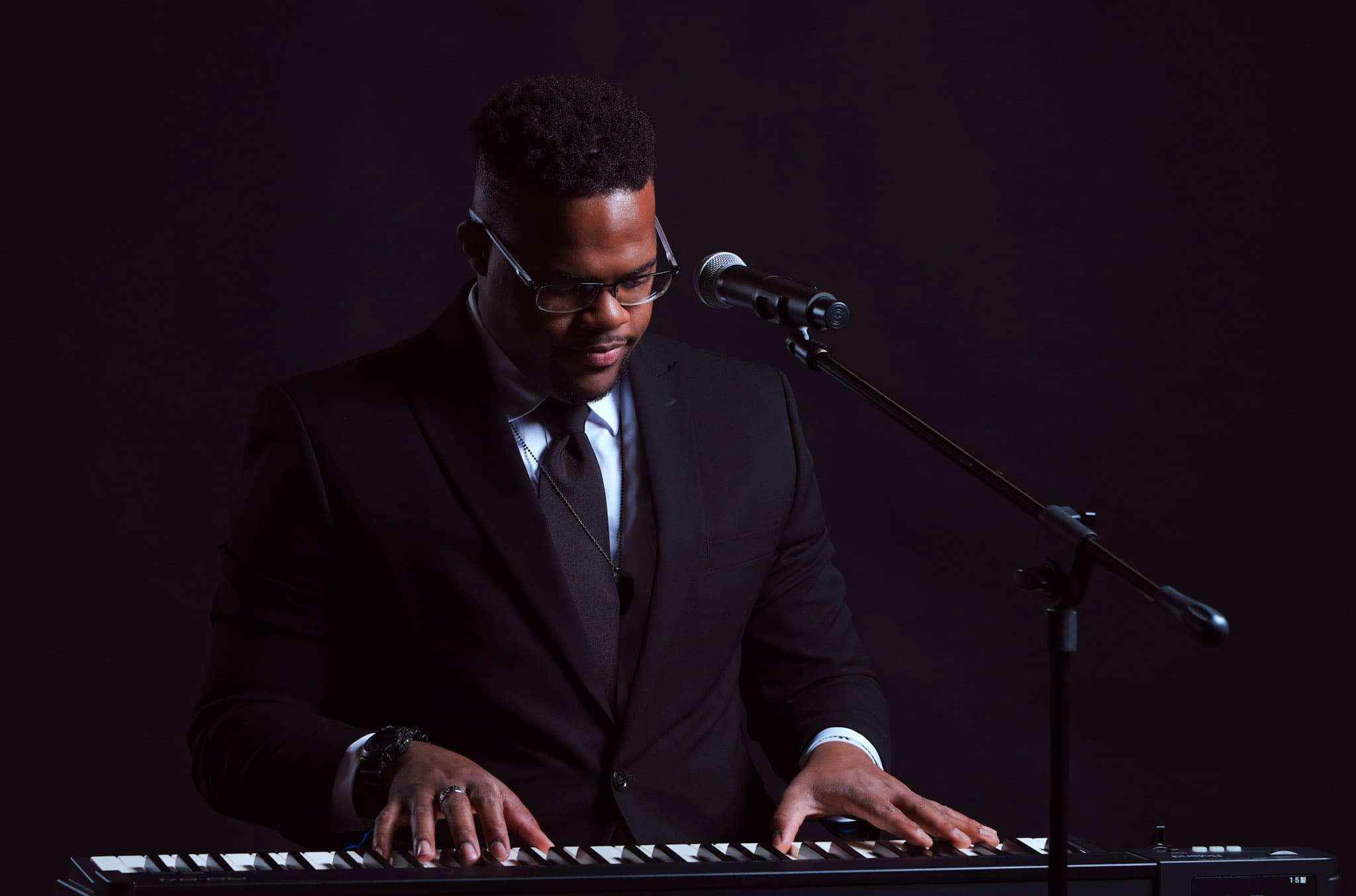 JKelly Music playing keyboard with a microphone in a professional studio setting
